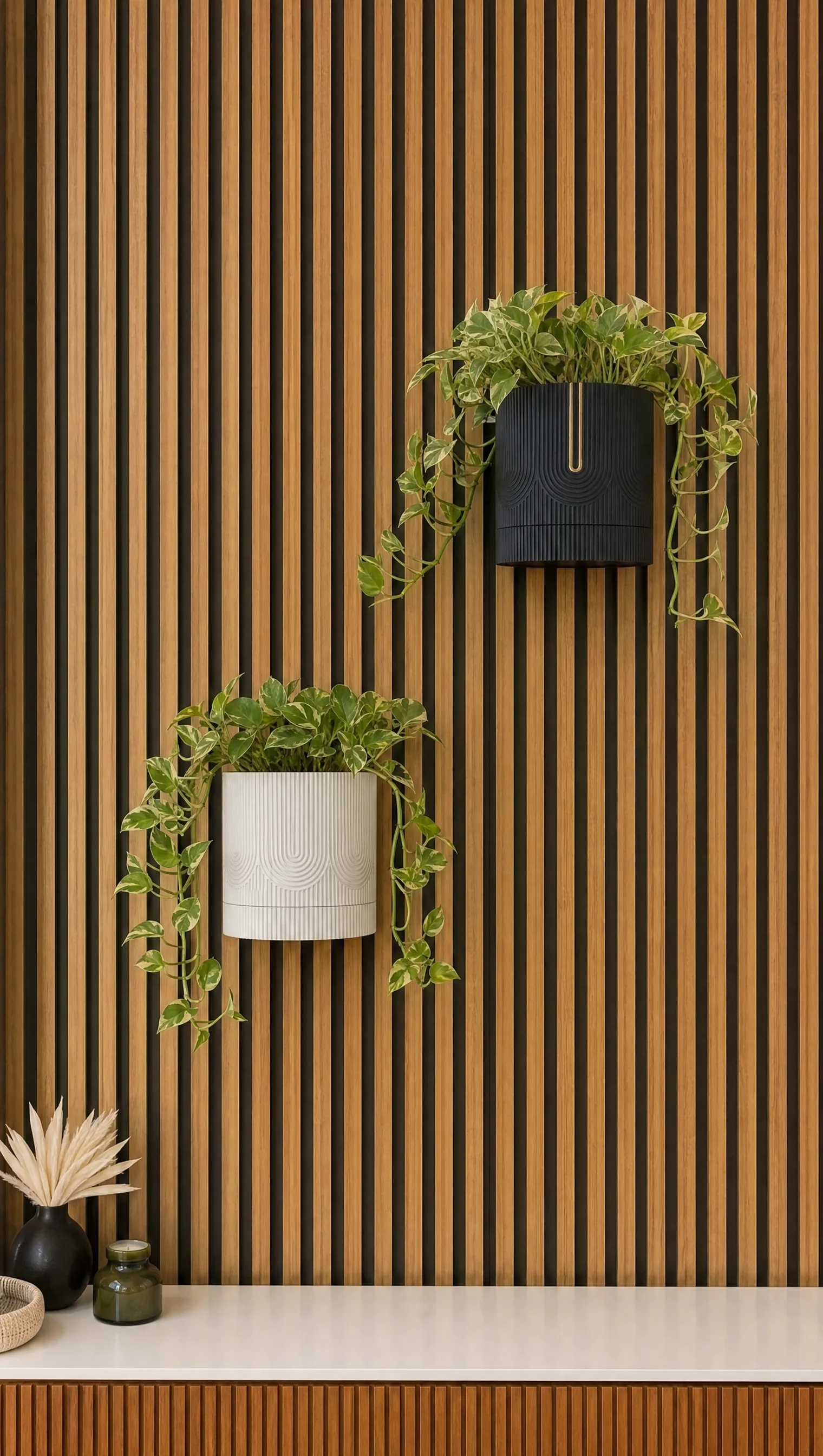 A black smart planter with a gold line and a white one below it, both with trailing pothos on a walnut slat wall